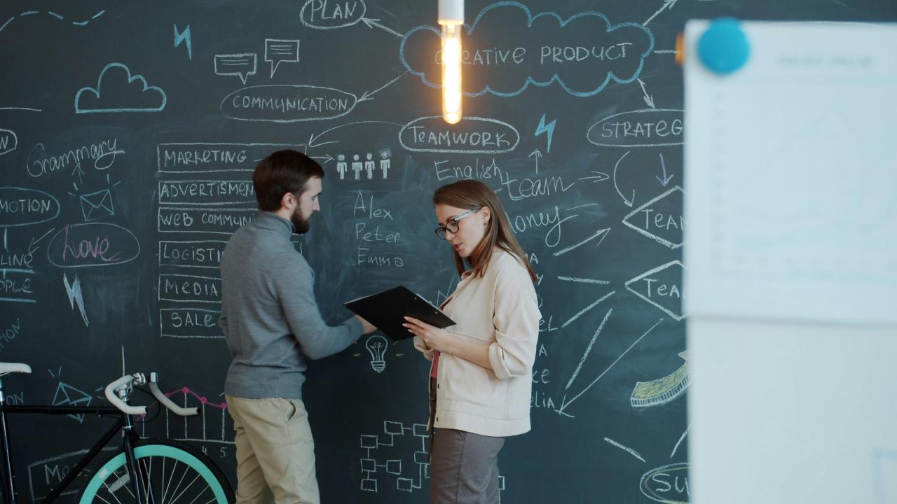 Two people discussing a business plan on chalkboard.