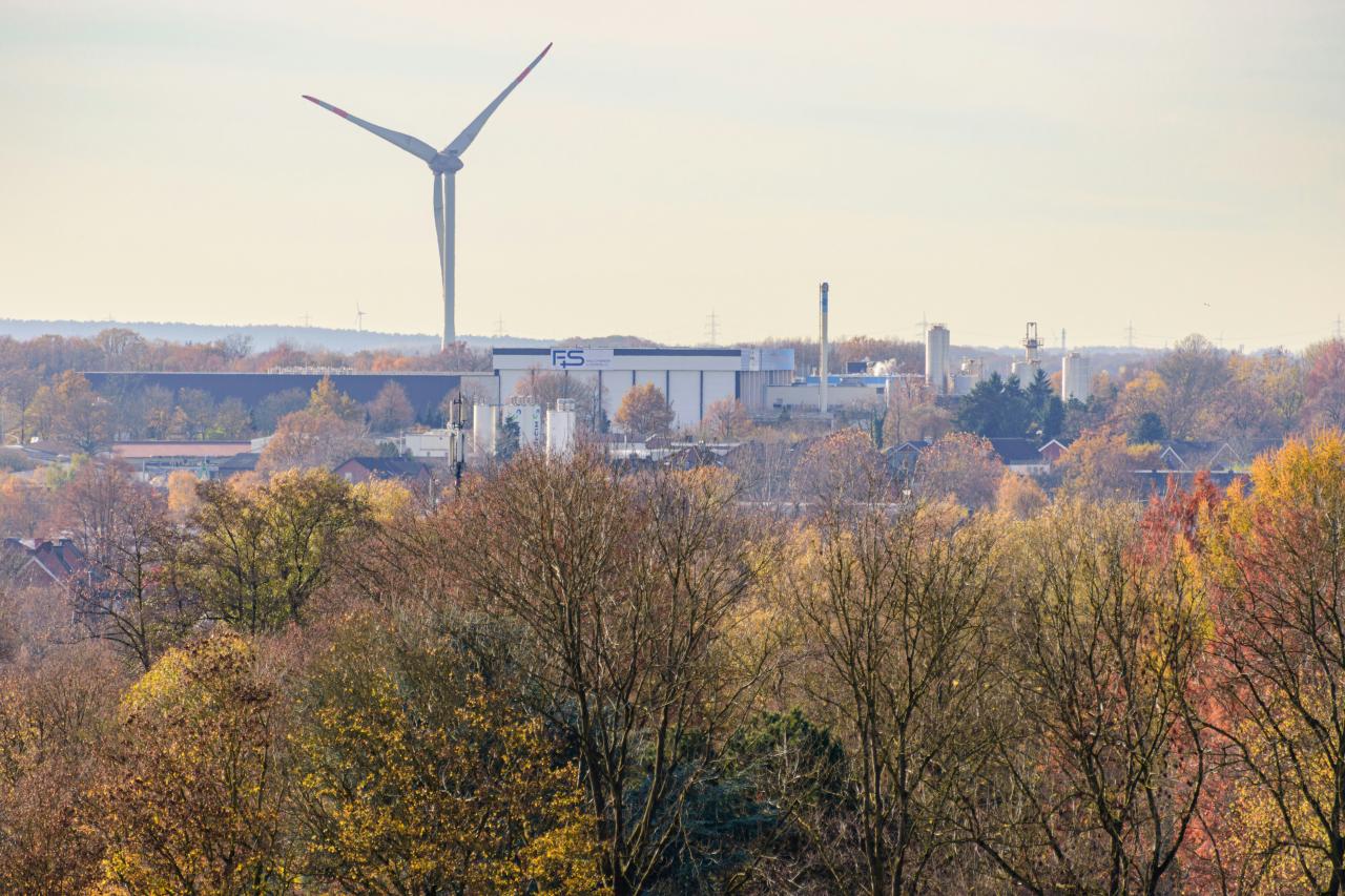 Wind turbine above autumn trees and industrial buildings